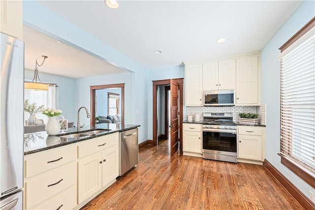 kitchen with appliances with stainless steel finishes, hardwood / wood-style flooring, decorative light fixtures, backsplash, and dark stone countertops