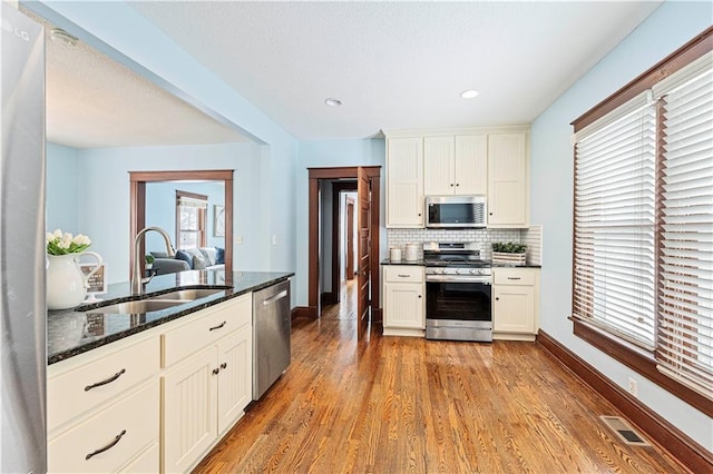 kitchen featuring stainless steel appliances, light hardwood / wood-style flooring, sink, tasteful backsplash, and dark stone counters