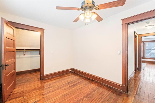 unfurnished bedroom with a spacious closet, a closet, ceiling fan, and wood-type flooring