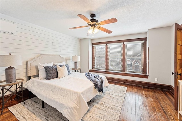 bedroom with a textured ceiling, wood walls, dark hardwood / wood-style floors, and ceiling fan