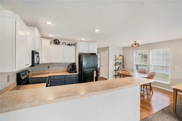 kitchen featuring light hardwood / wood-style floors, black appliances, white cabinets, decorative backsplash, and kitchen peninsula