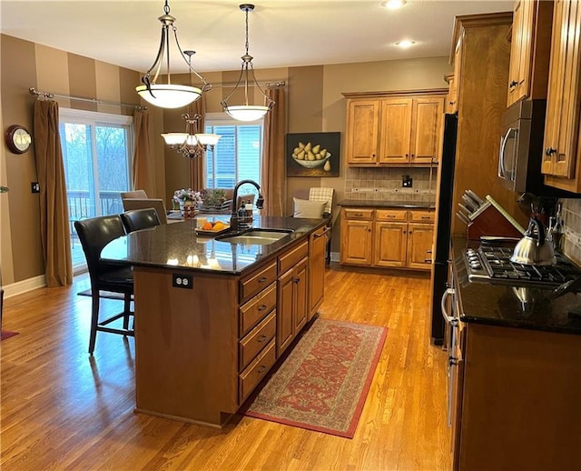 kitchen with sink, a breakfast bar, hanging light fixtures, a center island with sink, and light wood-type flooring