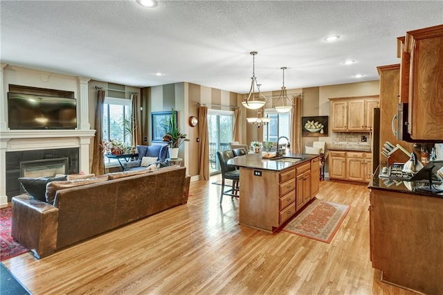 kitchen with pendant lighting, an island with sink, sink, a kitchen bar, and light wood-type flooring