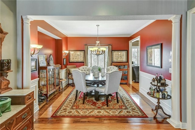 dining area featuring crown molding, light hardwood / wood-style flooring, decorative columns, and a chandelier