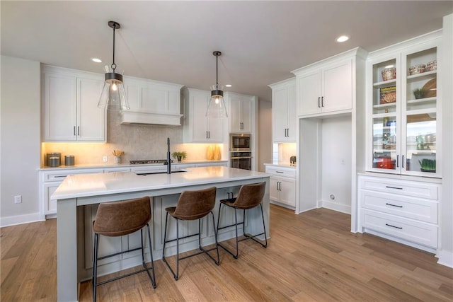 kitchen with pendant lighting, white cabinets, a center island with sink, light hardwood / wood-style floors, and stainless steel appliances