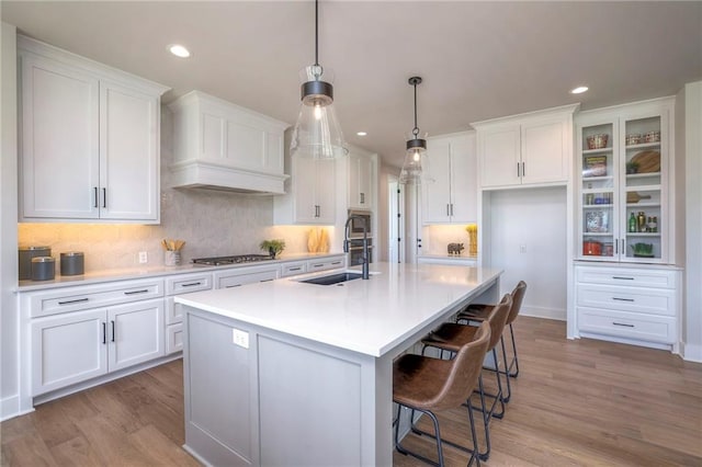 kitchen with stainless steel gas cooktop, sink, a center island with sink, white cabinets, and hanging light fixtures