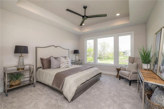 bedroom with a raised ceiling, ceiling fan, and light colored carpet