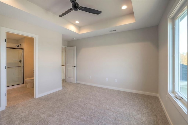 unfurnished bedroom with ensuite bathroom, a raised ceiling, ceiling fan, and light colored carpet