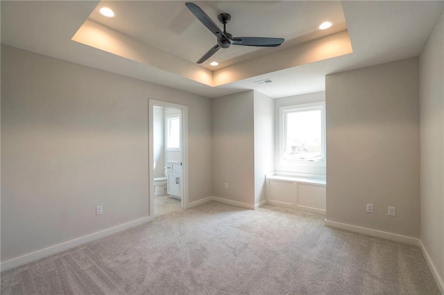 carpeted spare room featuring a raised ceiling, ceiling fan, and a healthy amount of sunlight