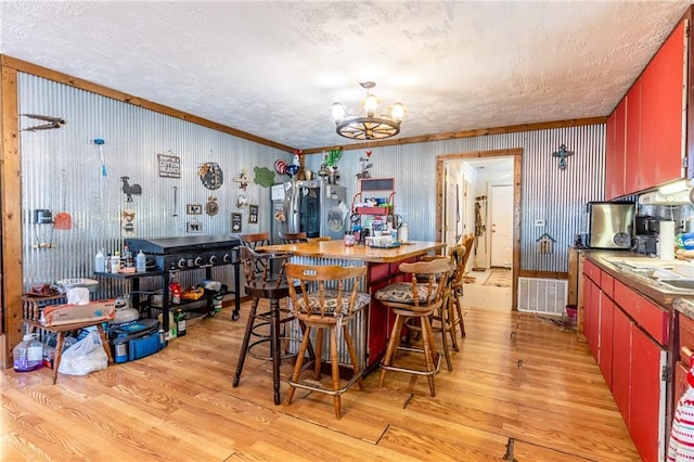 dining room with a textured ceiling, light wood-type flooring, an inviting chandelier, and crown molding