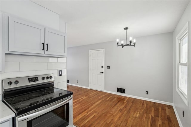 kitchen with a wealth of natural light, white cabinetry, an inviting chandelier, backsplash, and electric range