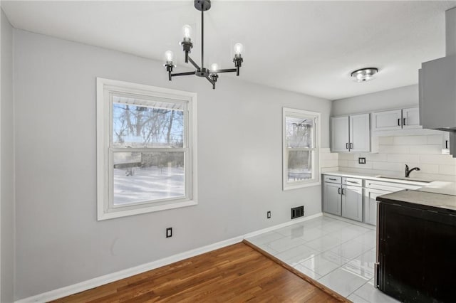 kitchen featuring decorative backsplash, gray cabinetry, a notable chandelier, hanging light fixtures, and sink