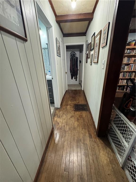 hall with wood walls, beamed ceiling, and wood-type flooring