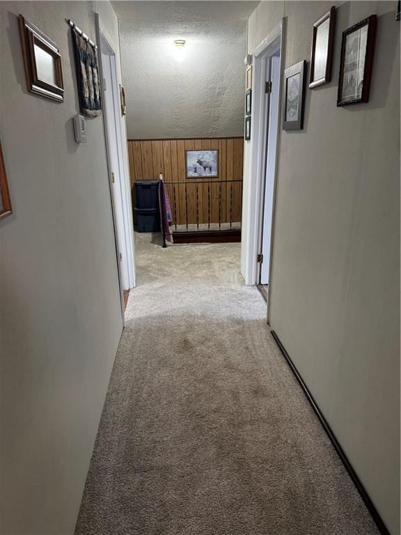 hall with light carpet, a textured ceiling, and wooden walls