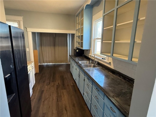 kitchen with decorative backsplash, black fridge, sink, dark hardwood / wood-style floors, and white cabinetry