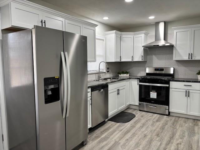 kitchen with white cabinetry, sink, stainless steel appliances, wall chimney range hood, and tasteful backsplash