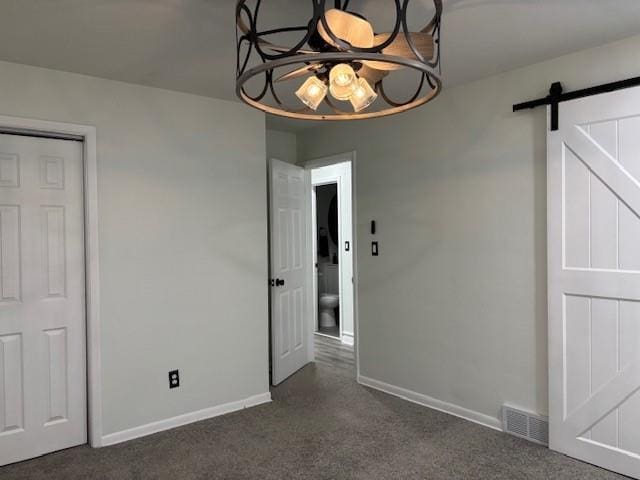 carpeted spare room featuring a barn door and a notable chandelier