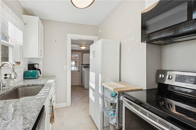 kitchen featuring white cabinetry, stainless steel appliances, light stone counters, washer / clothes dryer, and sink