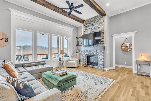 living room featuring ceiling fan, a stone fireplace, beam ceiling, and light hardwood / wood-style flooring