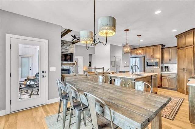 dining space with ceiling fan, sink, a fireplace, and light hardwood / wood-style flooring