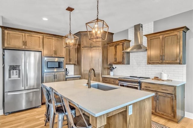 kitchen featuring appliances with stainless steel finishes, decorative light fixtures, a center island with sink, and wall chimney range hood