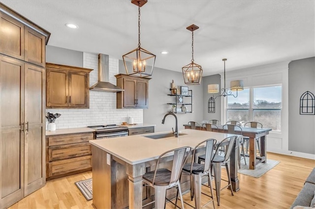 kitchen with wall chimney exhaust hood, a breakfast bar, sink, decorative light fixtures, and a center island with sink