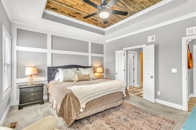 carpeted bedroom with a raised ceiling, crown molding, ceiling fan, and wood ceiling