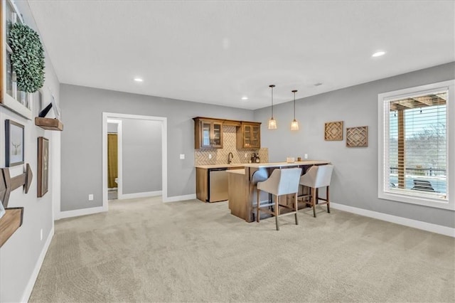 kitchen with pendant lighting, a breakfast bar, dishwasher, light carpet, and decorative backsplash