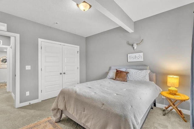 carpeted bedroom featuring beam ceiling and a closet