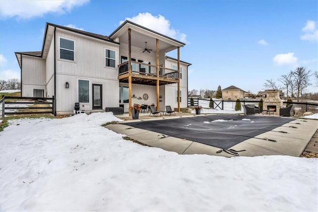 snow covered house with ceiling fan, a fireplace, a balcony, and a patio area