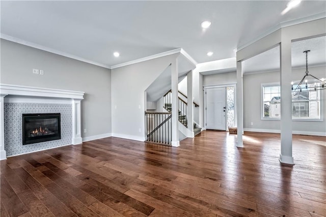 unfurnished living room featuring ornamental molding, dark hardwood / wood-style flooring, a tiled fireplace, and a notable chandelier