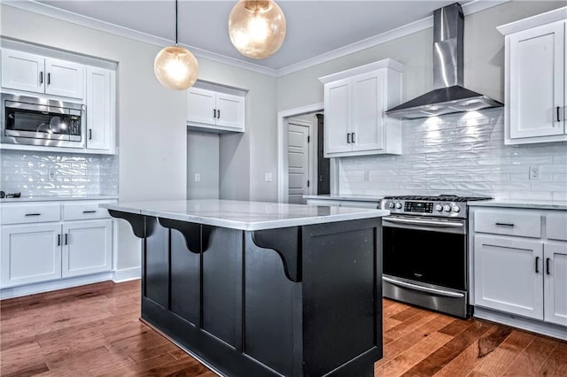 kitchen with appliances with stainless steel finishes, white cabinetry, a center island, decorative light fixtures, and wall chimney exhaust hood