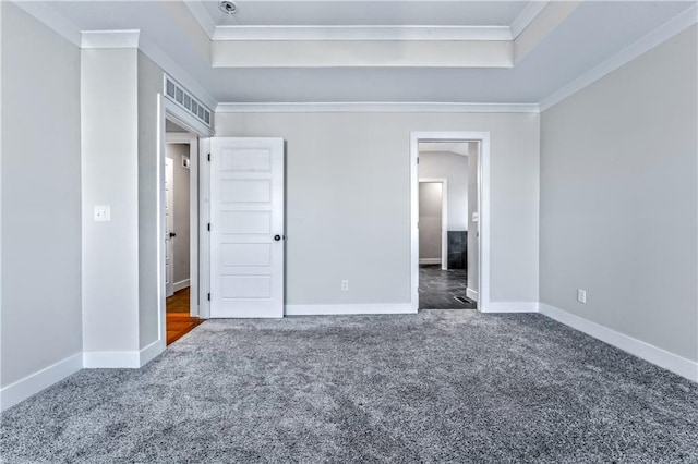 unfurnished bedroom featuring ensuite bath, ornamental molding, a tray ceiling, and dark carpet