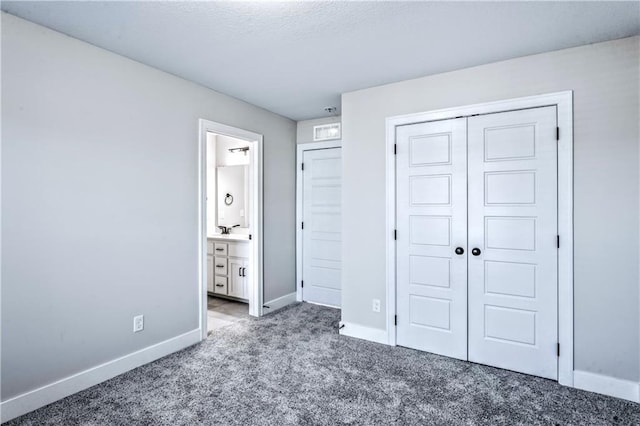 unfurnished bedroom featuring sink, dark carpet, ensuite bath, and a closet