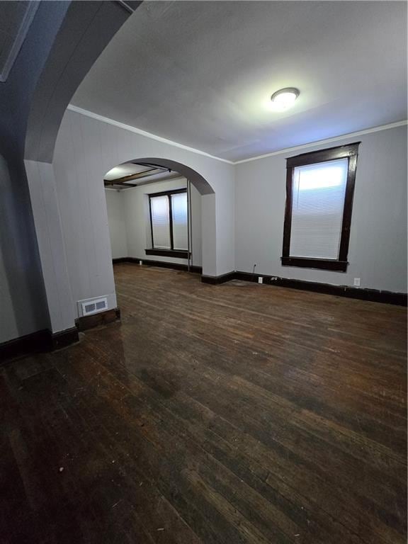 spare room with baseboards, visible vents, arched walkways, ornamental molding, and dark wood-type flooring