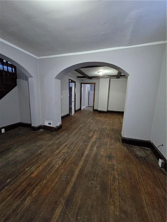 empty room with arched walkways, ornamental molding, wood finished floors, and baseboards