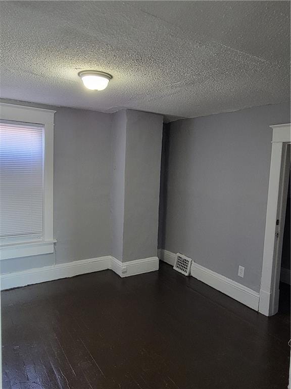 unfurnished room with visible vents, a textured ceiling, baseboards, and dark wood-style flooring