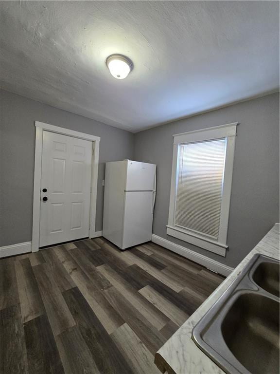 kitchen with dark wood-type flooring, a sink, freestanding refrigerator, and baseboards