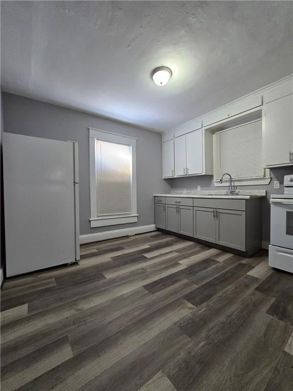 kitchen with dark wood-style floors, light countertops, gray cabinetry, a sink, and white appliances