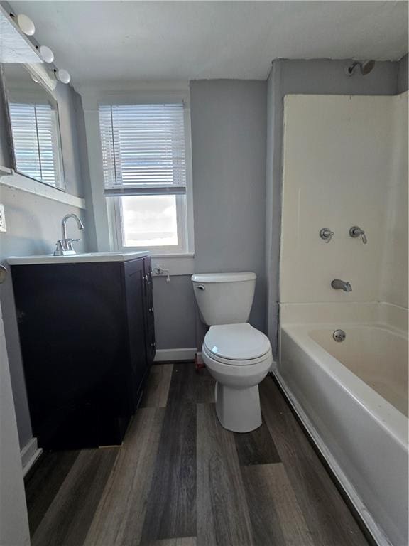 bathroom featuring baseboards, toilet, wood finished floors,  shower combination, and vanity