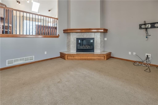 unfurnished living room featuring a tile fireplace, carpet floors, and a skylight