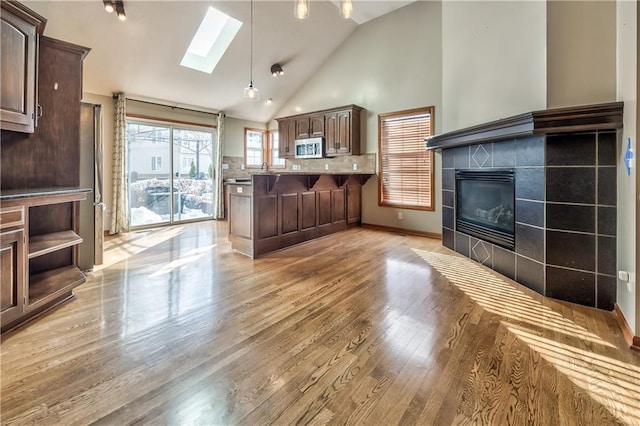 living room with high vaulted ceiling, light wood-type flooring, a skylight, and a fireplace