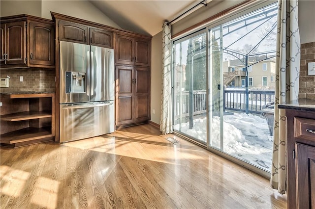 kitchen with stainless steel refrigerator with ice dispenser, lofted ceiling, dark brown cabinets, and tasteful backsplash