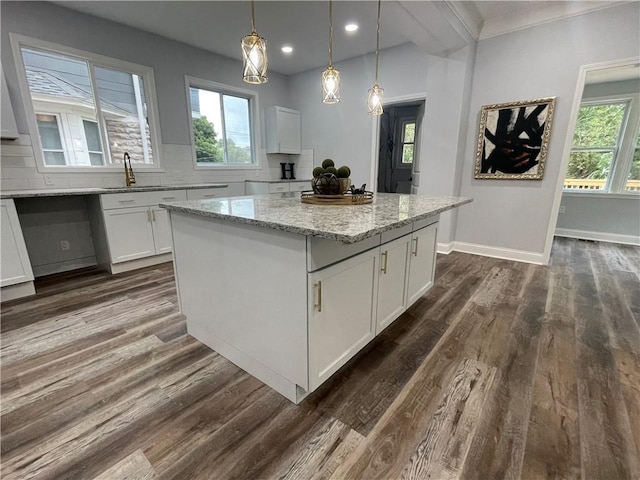 kitchen with hanging light fixtures, a kitchen island, light stone counters, backsplash, and white cabinets