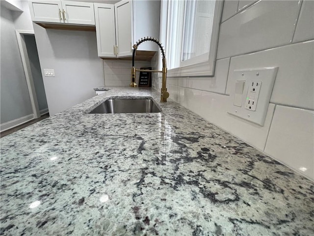 kitchen with light stone countertops, white cabinets, tasteful backsplash, and sink