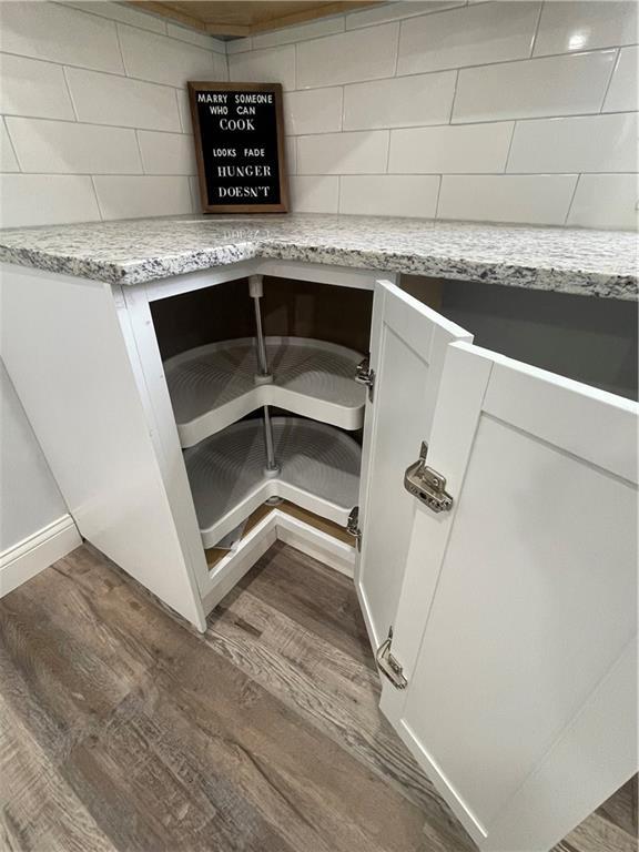 interior details with white cabinets, decorative backsplash, dark hardwood / wood-style floors, and light stone counters