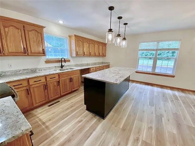 kitchen with pendant lighting, sink, light hardwood / wood-style flooring, light stone countertops, and a kitchen island