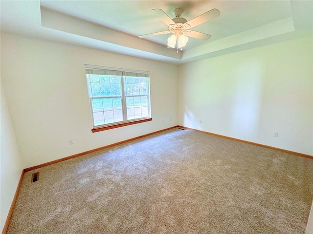 spare room featuring carpet flooring, a tray ceiling, and ceiling fan