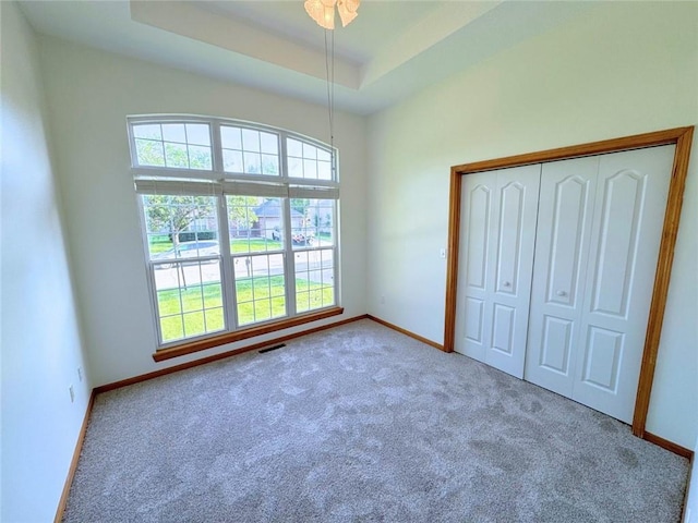 unfurnished bedroom with a tray ceiling, a closet, and light colored carpet