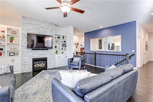 living room with dark wood-type flooring, ceiling fan, a fireplace, and built in features